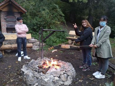 Drei Personen stehen um Grillstelle mit Stöcken herum